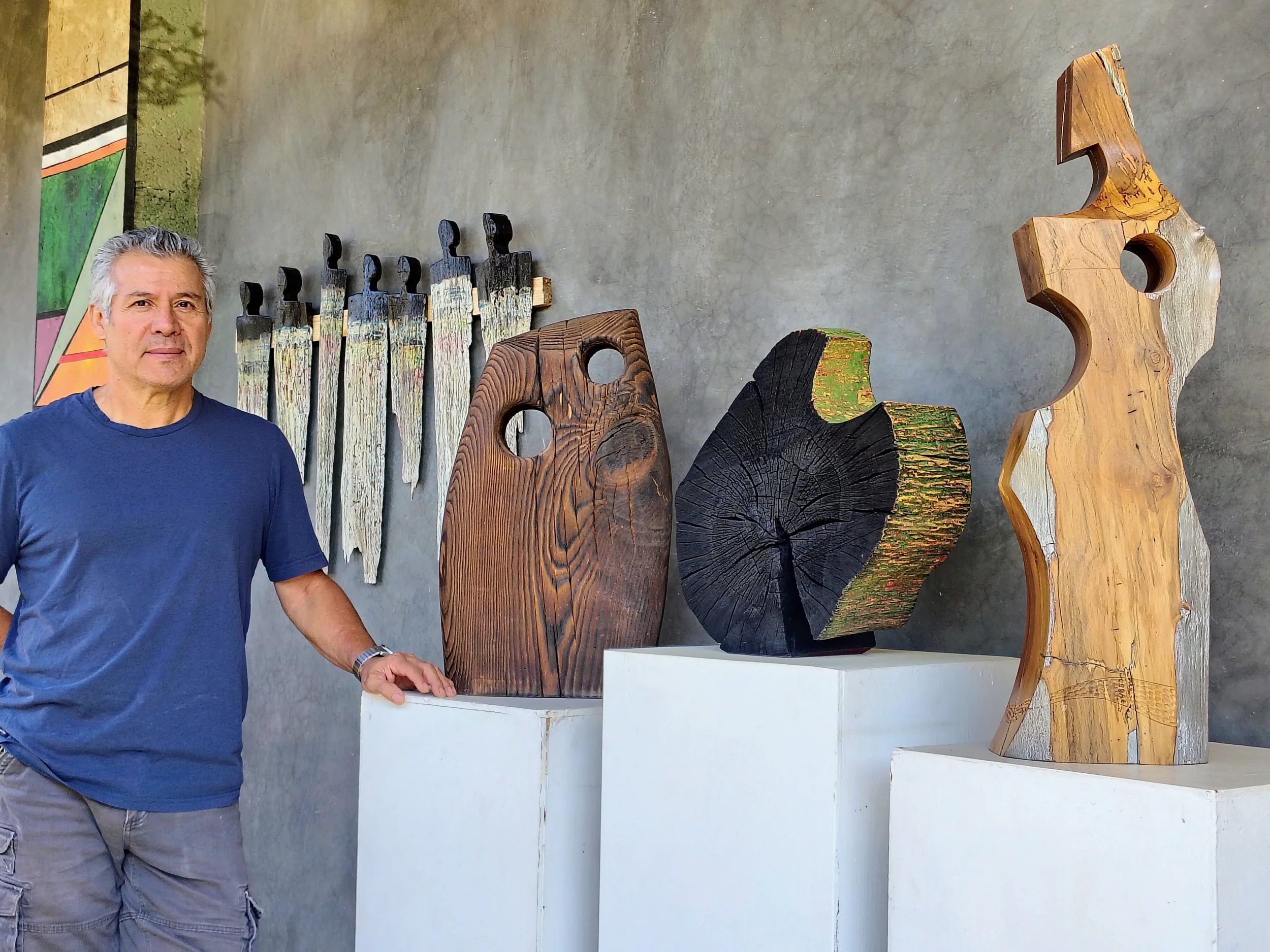 Gaspar Téllez standing beside his handcrafted wooden sculptures in his studio, showcasing his original wood designs.