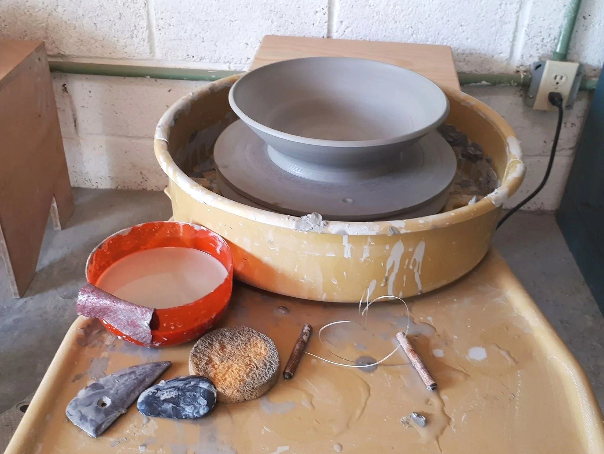 Pieza de cerámica recién torneada junto a herramientas de trabajo en un torno de cerámica.