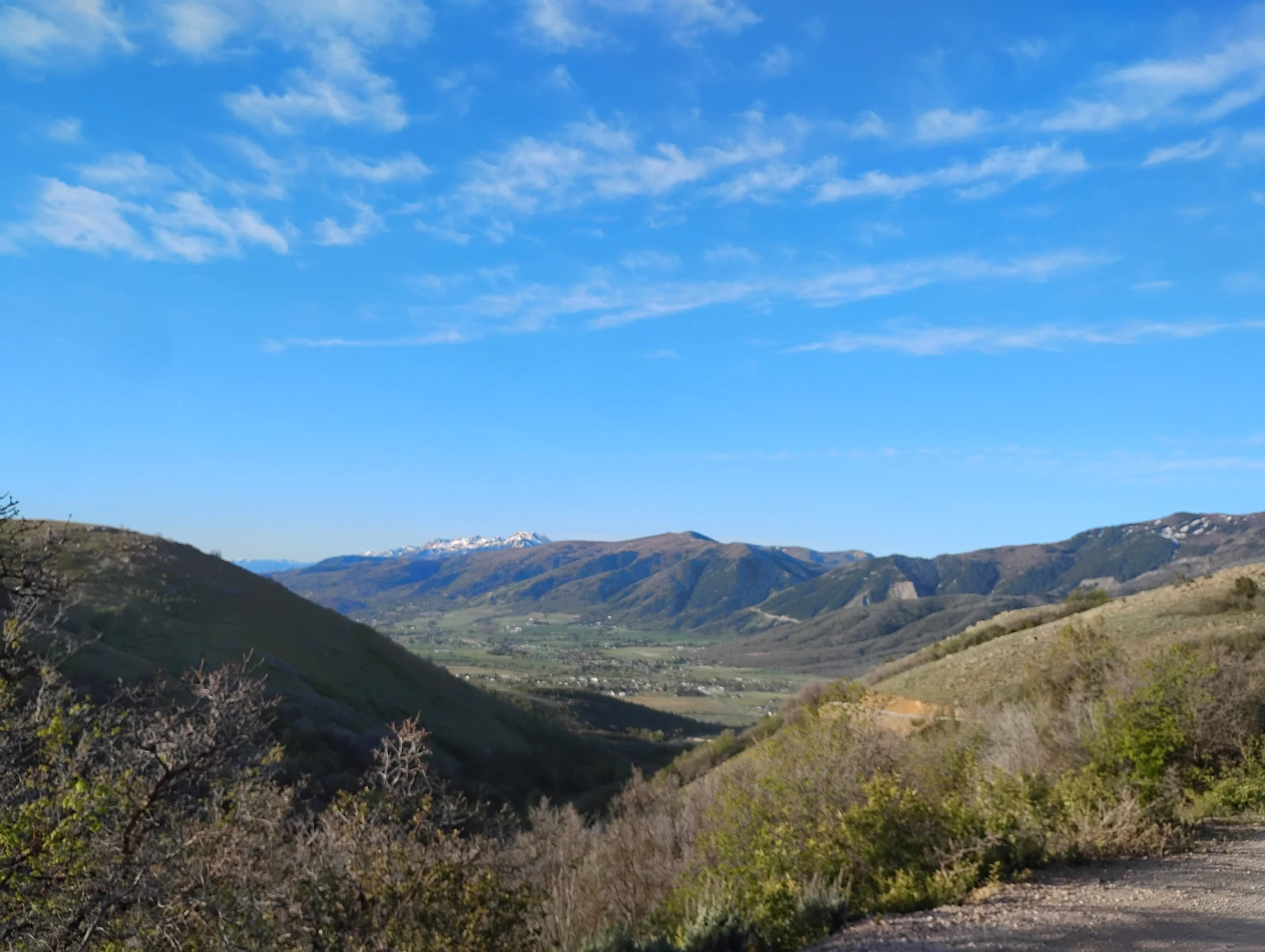 Scenic view of rolling hills and mountains under a blue sky with scattered clouds.