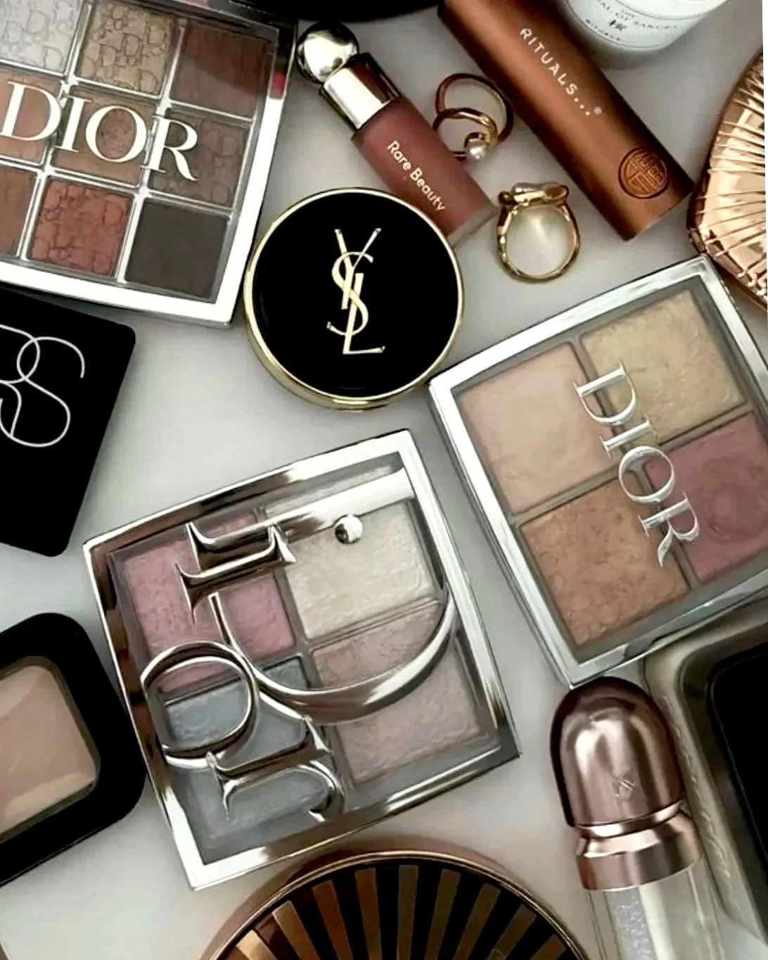 Collection of makeup products including Dior and Yves Saint Laurent palettes, and other beauty products.