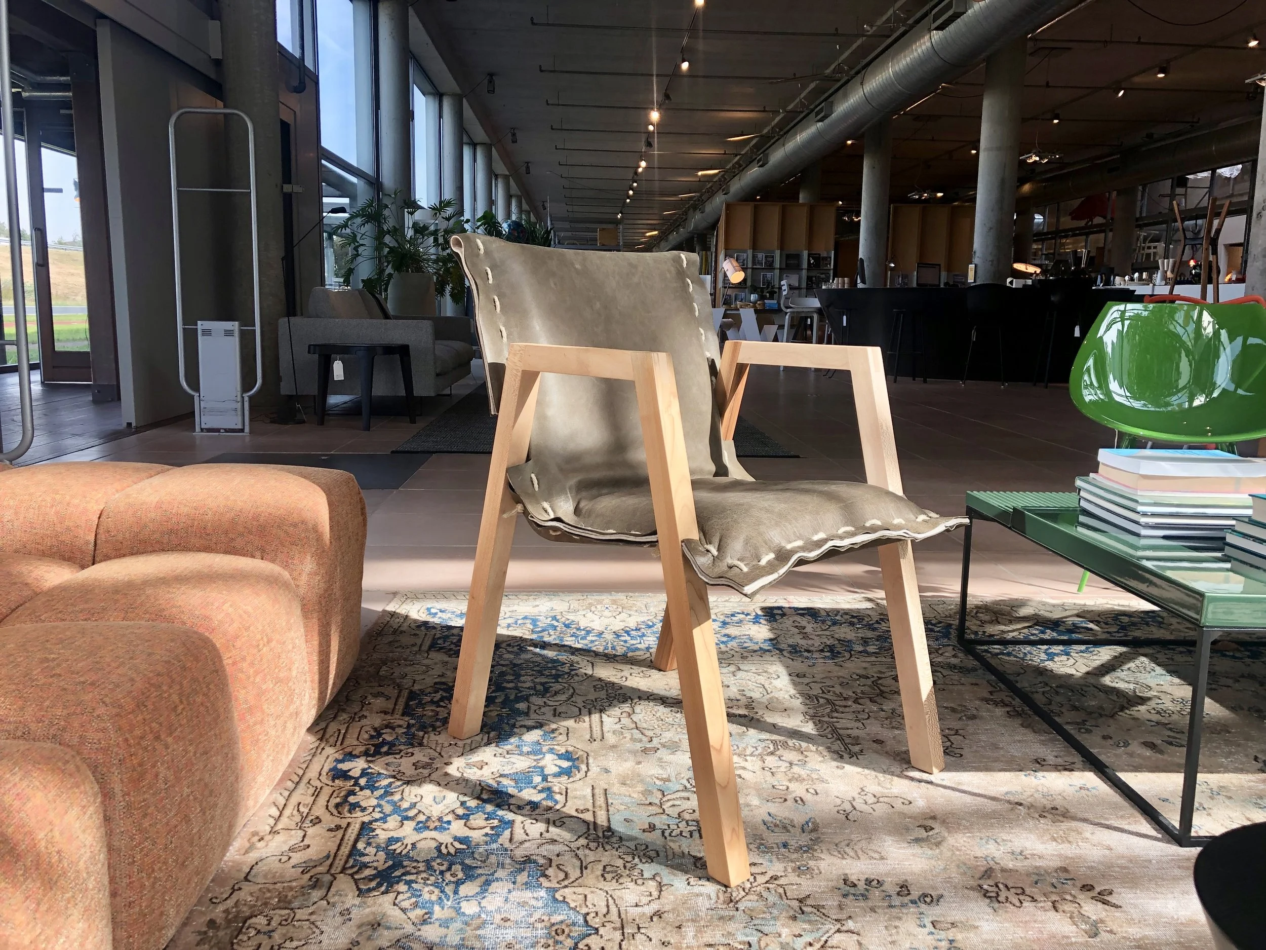 Interieur van een modern gebouw met grote ramen, fauteuils, tafels, planten en decoratie, met een industriële uitstraling.