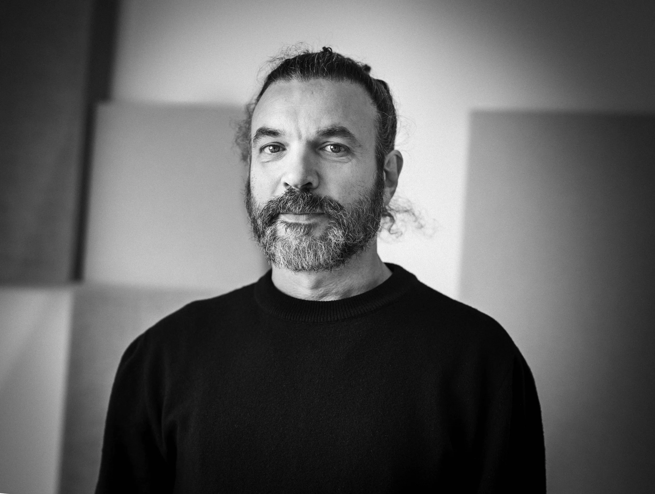 Een zwart-wit portret van een man met een baard en lange haar in een staand camerastandpunt.