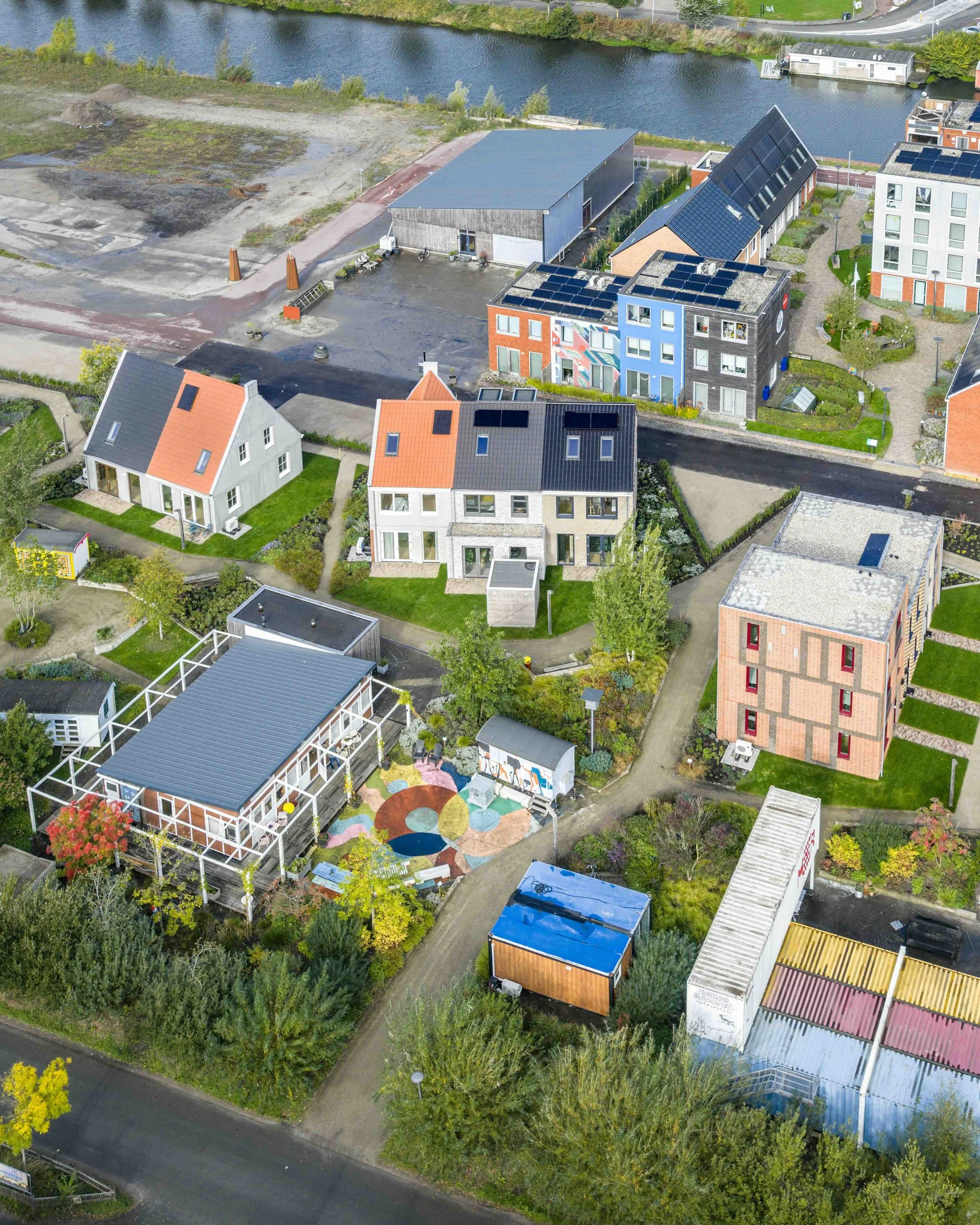 Luchtfoto van een woonwijk met huizen, een weg, een waterrivier en een groene omgeving, waaronder bomen en grasvelden.