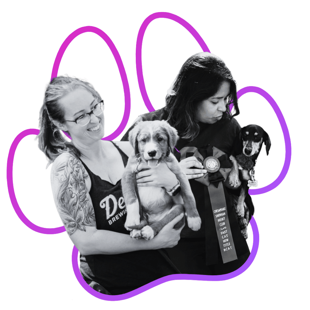 Two women (Terra and Jade of Wholistic Canine) holding puppies, one with glasses and tattoos, the other wearing a ribbon and badge, with gradient paw print outline around them.