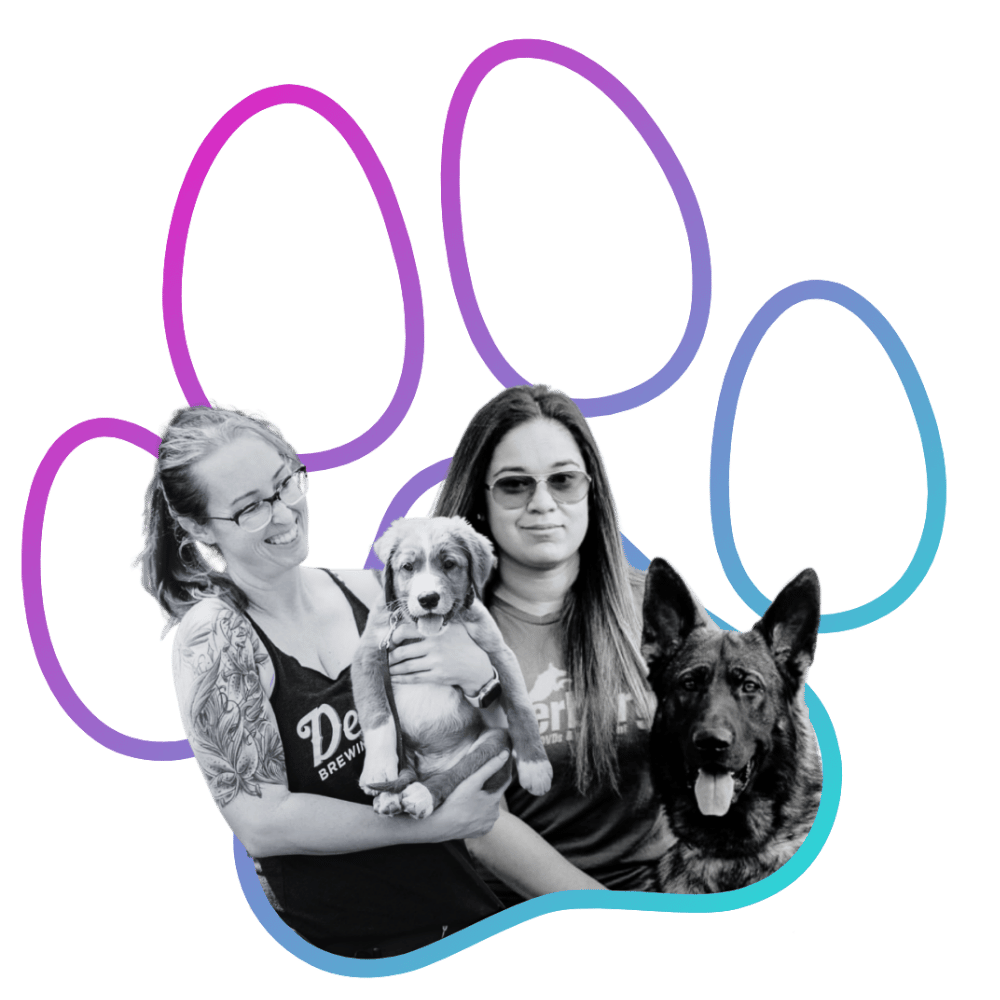Two women (Terra and Alex of Wholistic Canine) with tattoos and glasses holding two dogs, one small puppy and one larger German Shepherd, against a black background with colorful paw print outline.