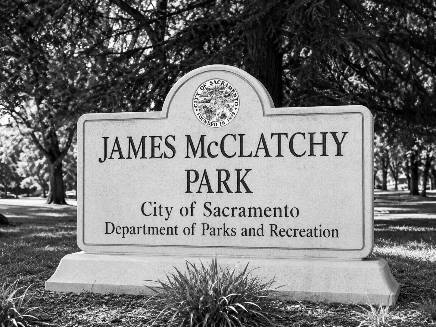 A black and white photograph of a sign for James McClatchy Park in Sacramento, California, with trees in the background.