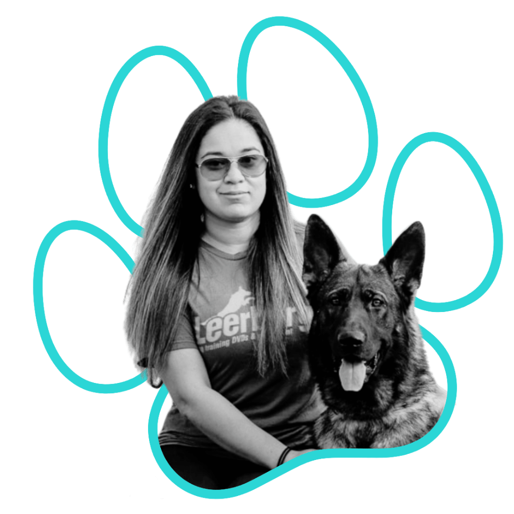 Black and white photo of a woman (Alex, Canine Relationship Coach for Wholistic Canine) with long hair, sunglasses, and a T-shirt, sitting with a German Shepherd dog. Blue outline of a paw print surrounds them.