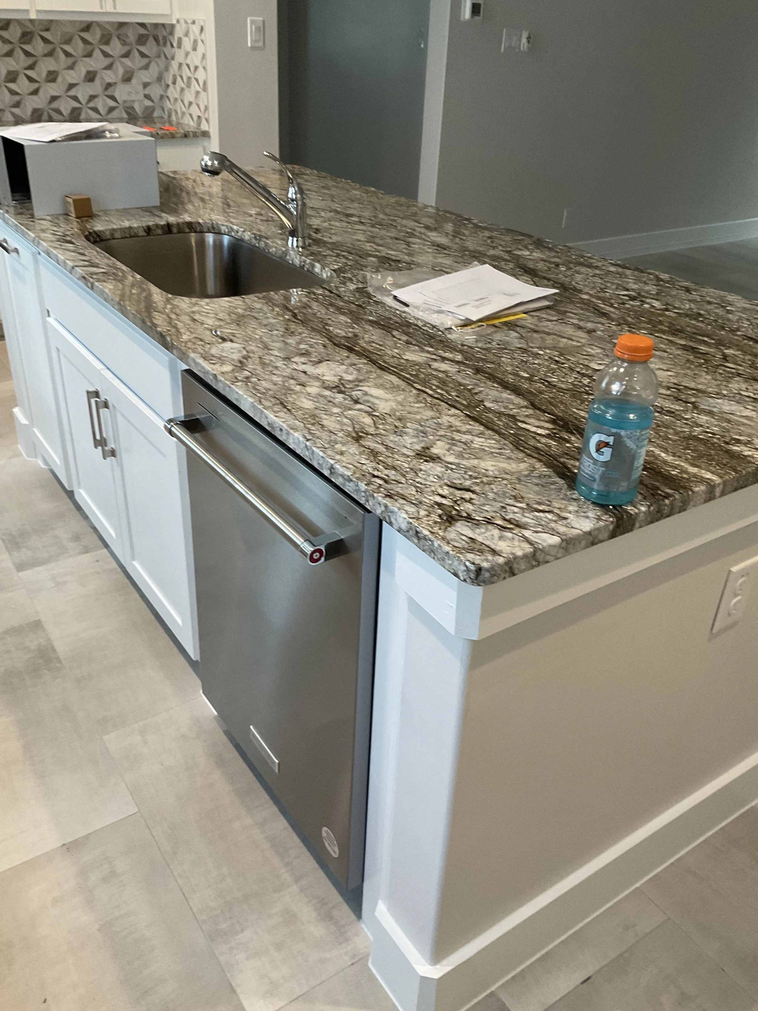 Kitchen island with granite countertop, stainless steel sink, faucet, a bottle of blue Gatorade, and papers on top.