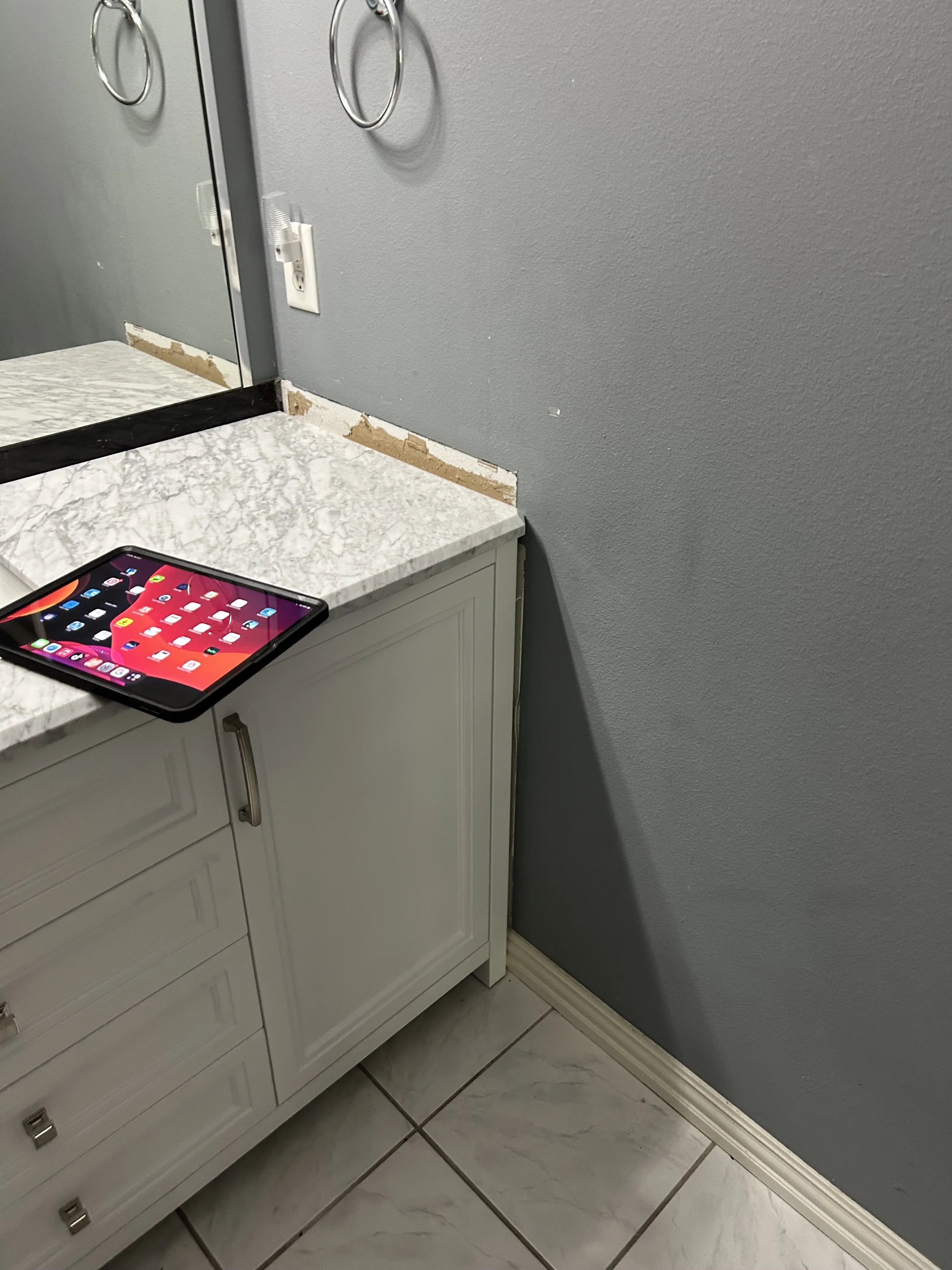 Bathroom vanity with a marble countertop, partially installed mirror, and electrical outlet. There is drywall work needed at the backsplash area.