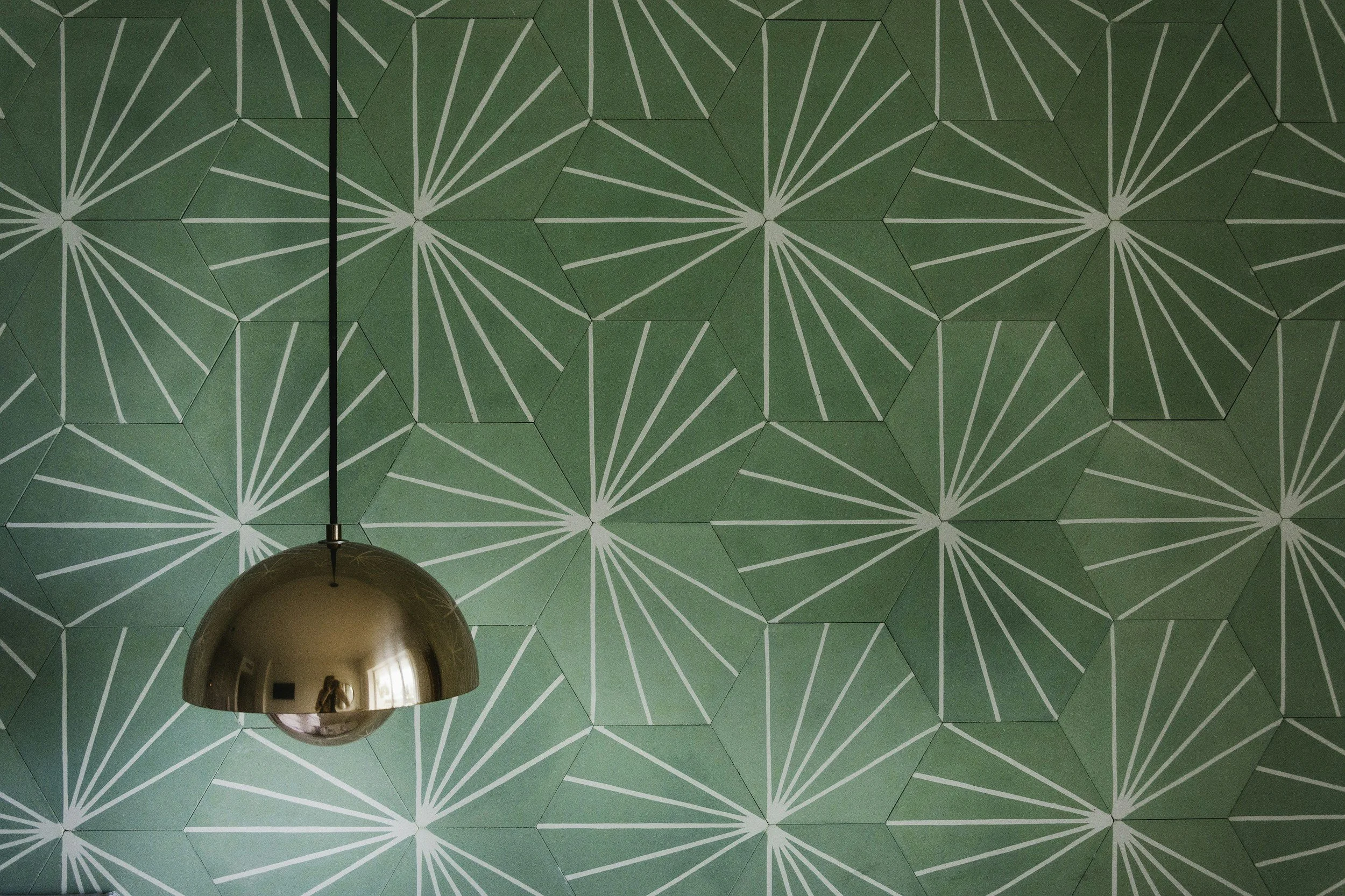 Wallpaper with geometric pattern of hexagons and radiating lines, partially obscured by a shiny, metallic spherical pendant light hanging from the ceiling.