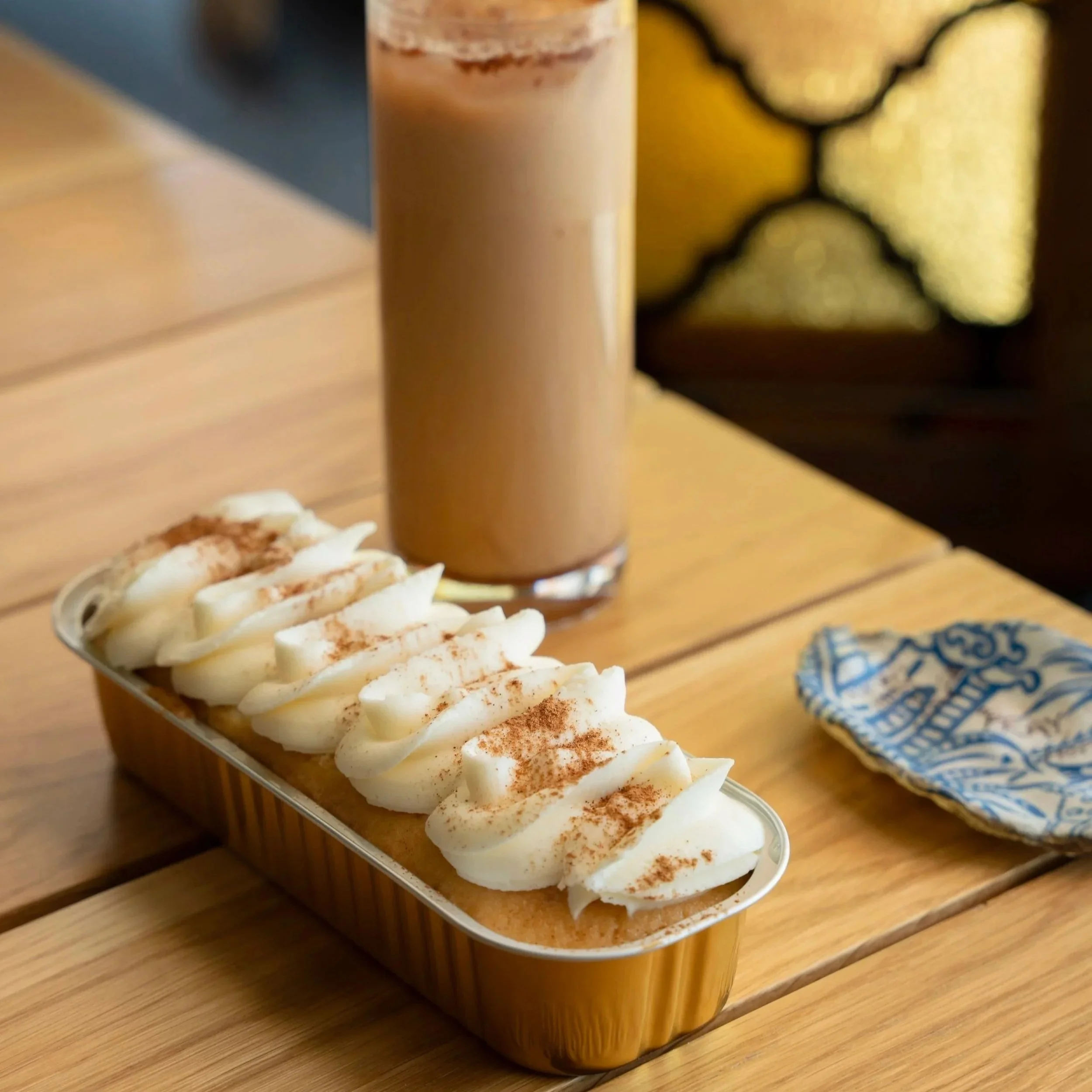 A dessert topped with whipped cream and a chocolate sprinkle alongside a glass of iced coffee on a wooden table.