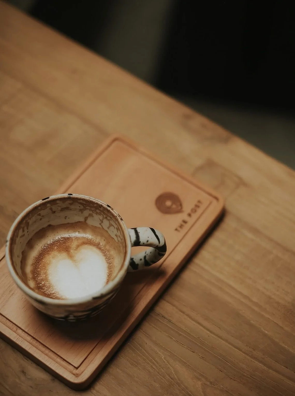 A ceramic coffee mug with a black and white striped pattern, containing a small amount of coffee foam, placed on a wooden tray on a wooden table.
