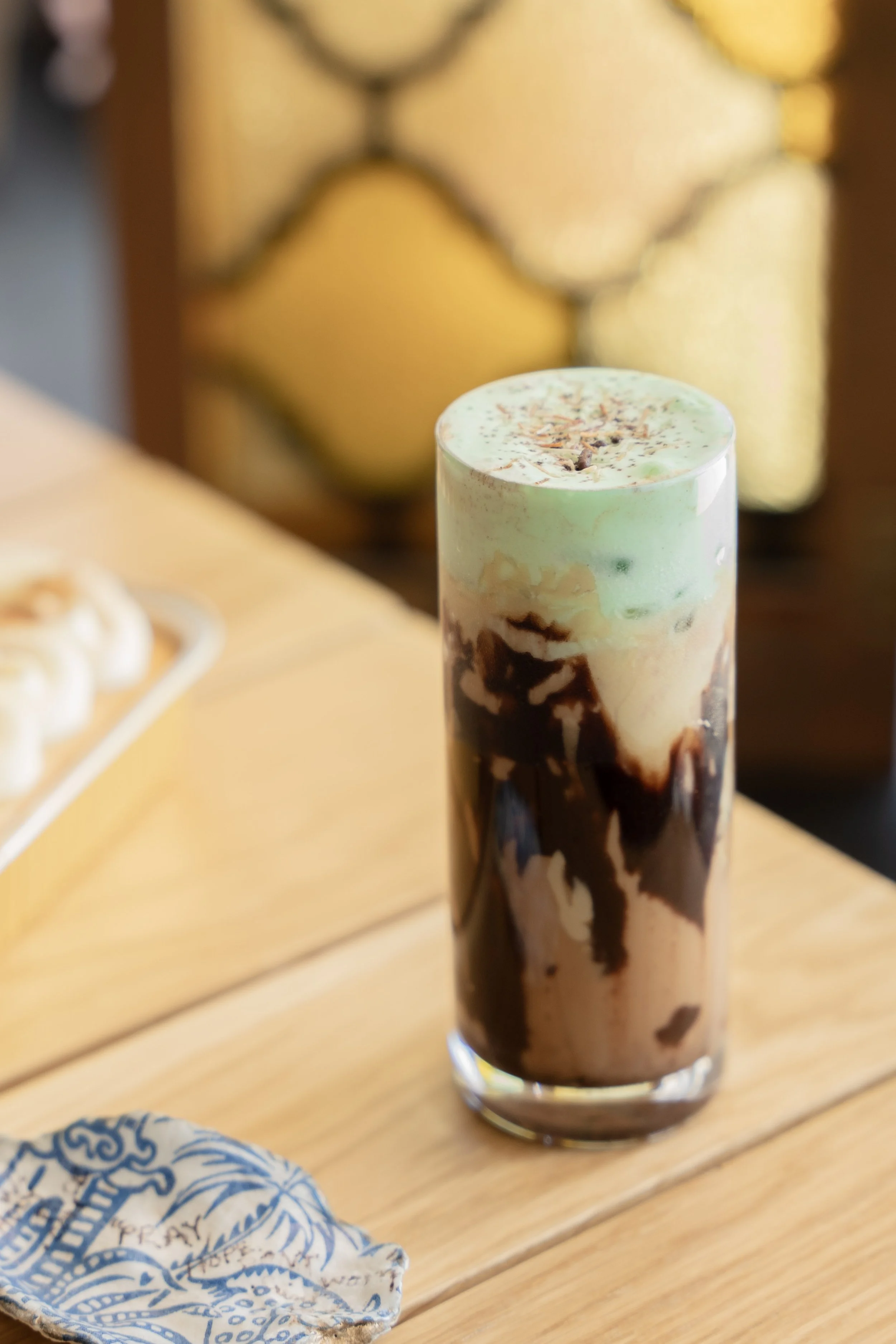 Tall glass of iced coffee with whipped cream, chocolate syrup, and green mint topping on a wooden table.