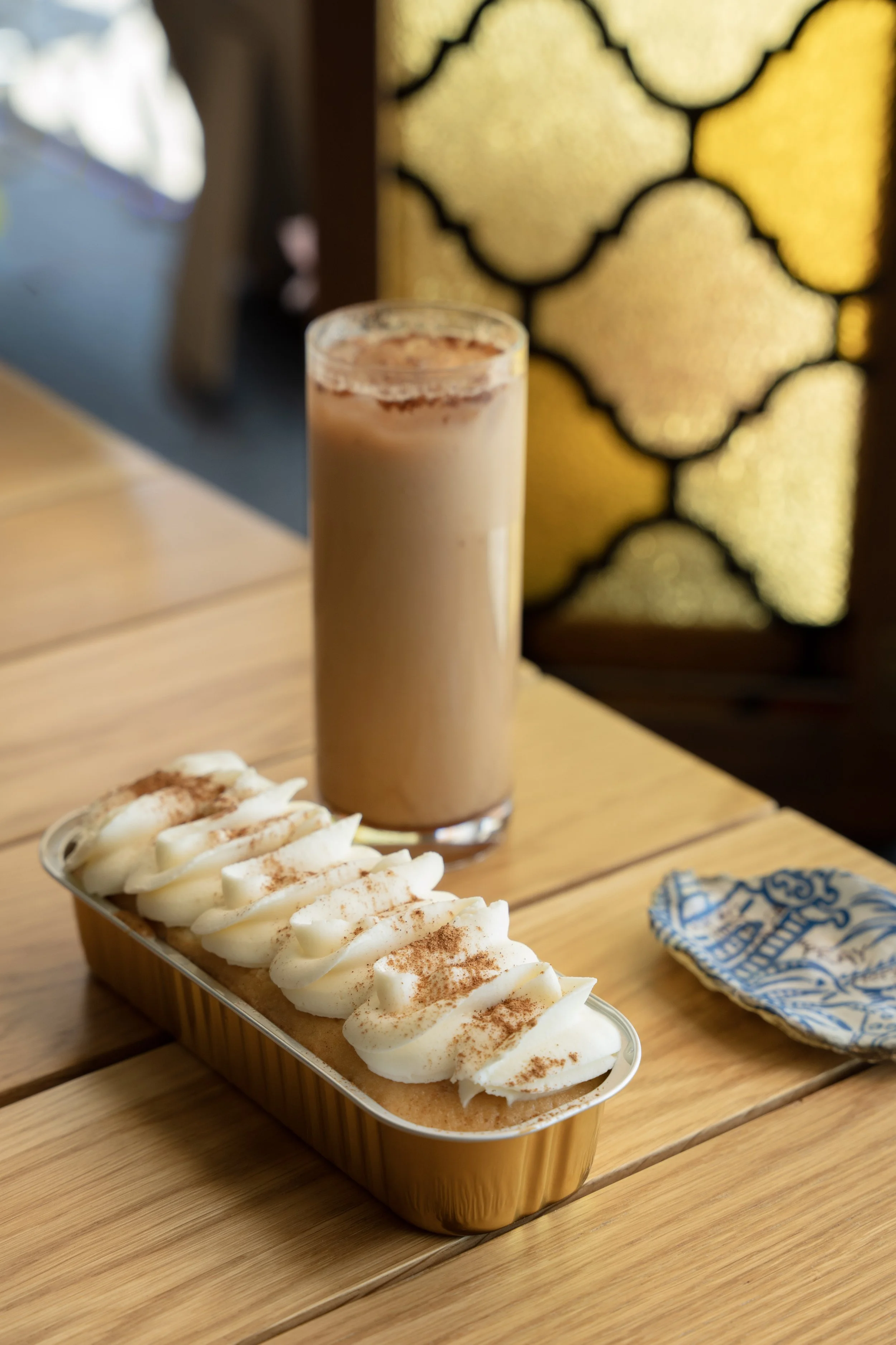 A glass of iced coffee or chocolate drink and a loaf of bread topped with whipped cream and cinnamon on a wooden table.