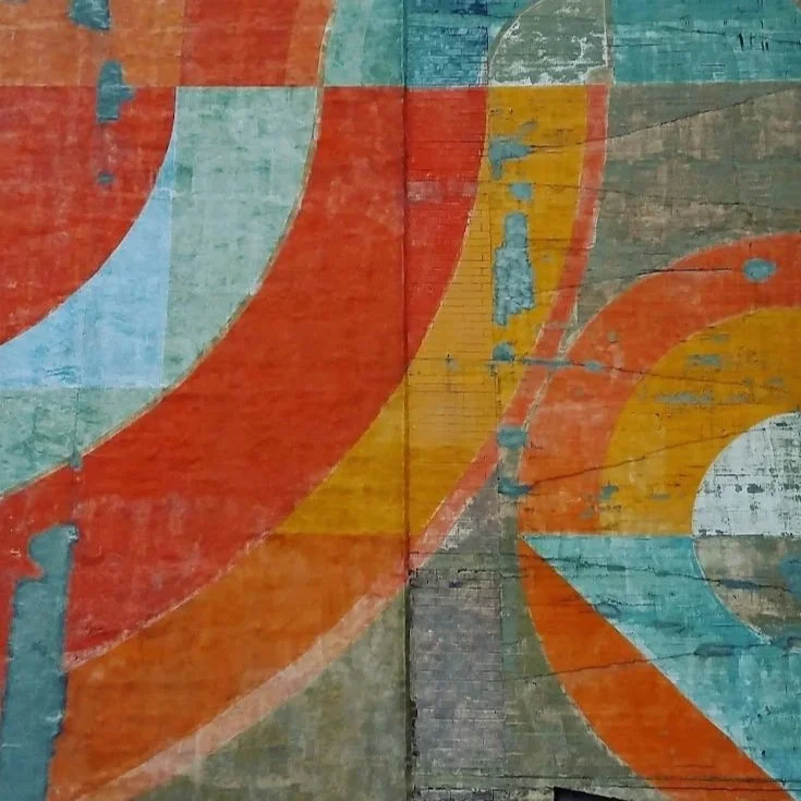 Close-up of a colorful abstract mural painted on a textured wooden wall with overlapping curved shapes in orange, blue, yellow, and green.
