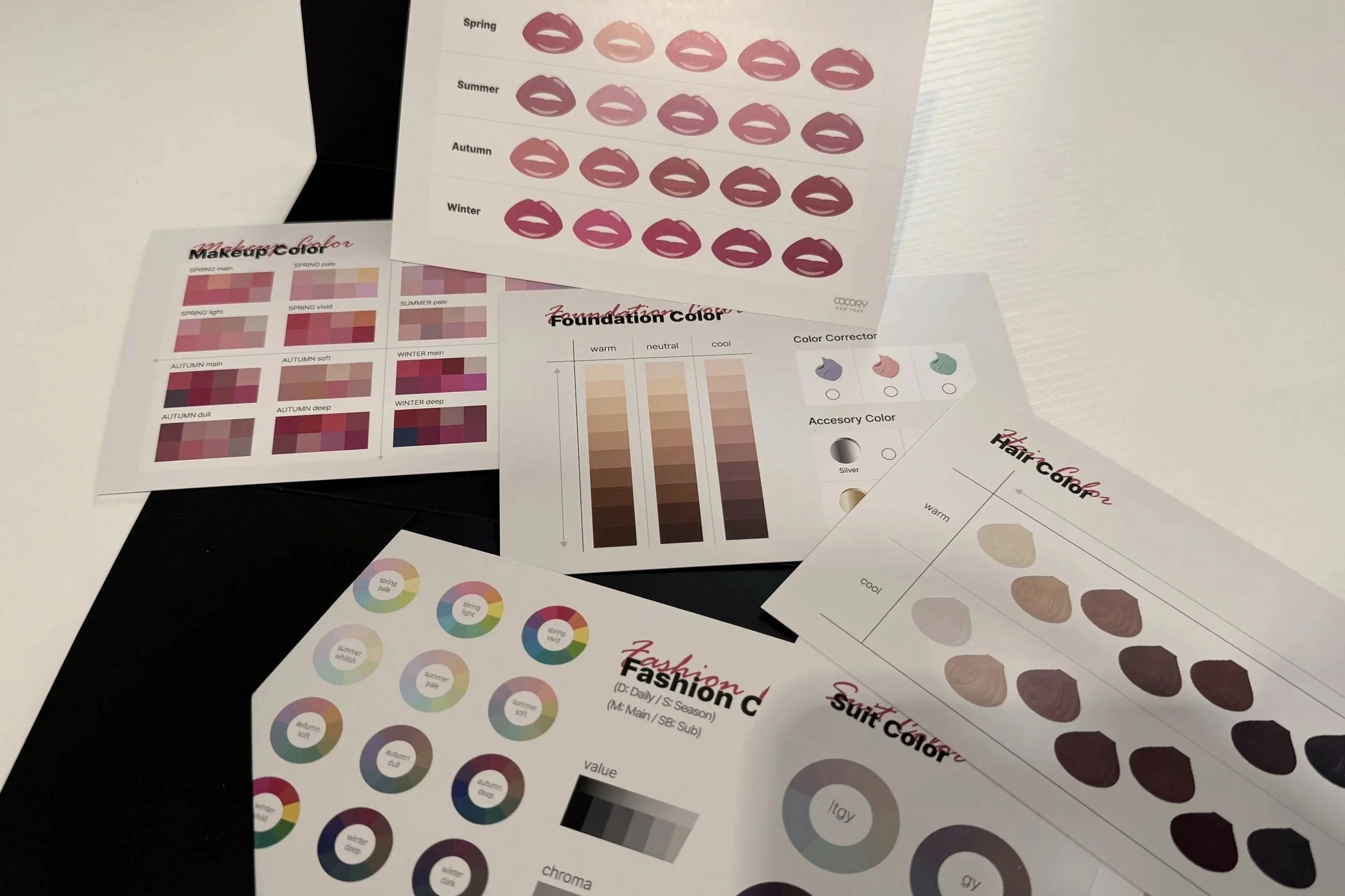 Various color samples and charts related to makeup, fashion, and hair color, including seasonal and foundation color guides, arranged on a table.