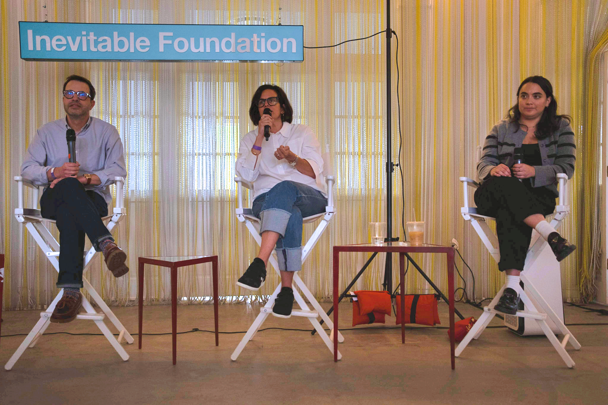 Three people sit in director’s chairs in front of an "Inevitable Foundation" sign as part of a panel discussion.