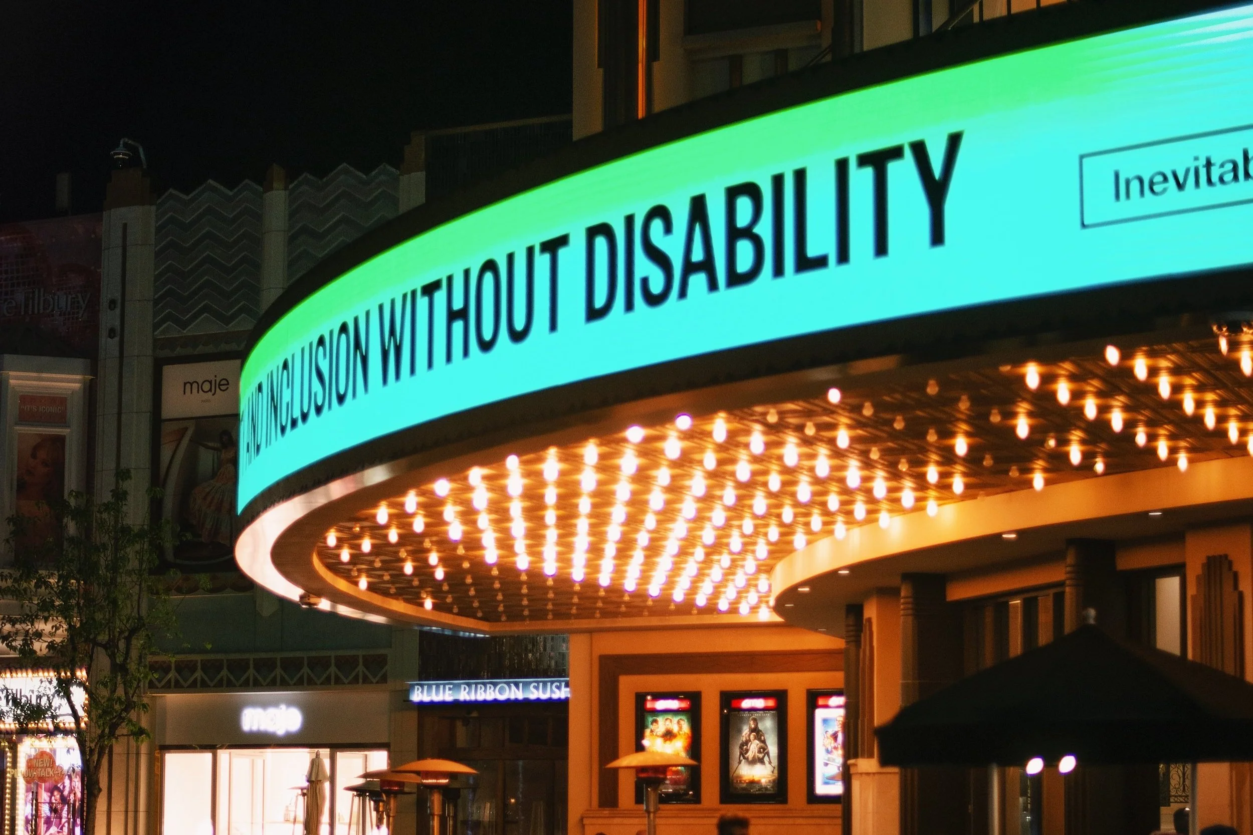A photo of a movie theater entrance at night, with a blue-green digital banner across the header and many glowing light bulbs facing down from the bottom of the entranceway roof.