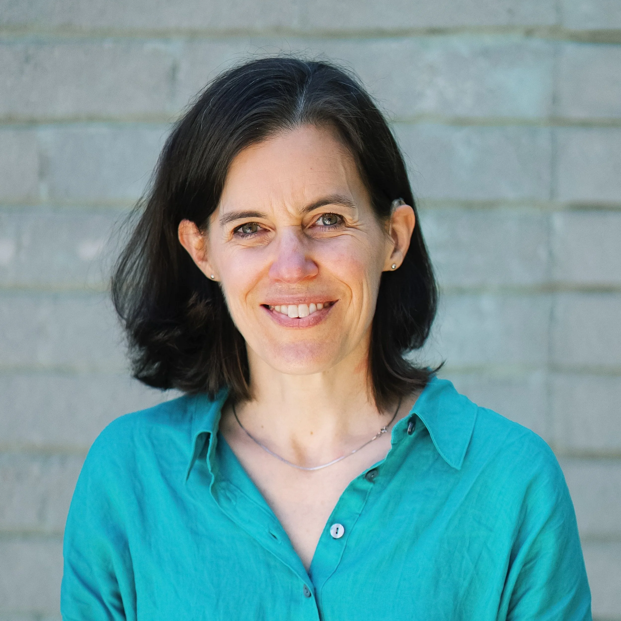 A smiling white woman with short brown hair and wearing a teal shirt.