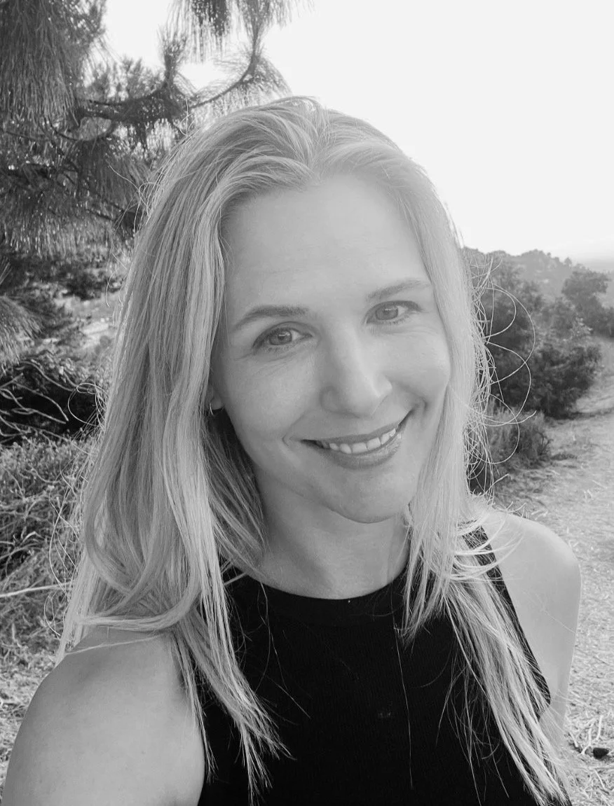 A black and white photo of a blonde person smiling directly into camera.