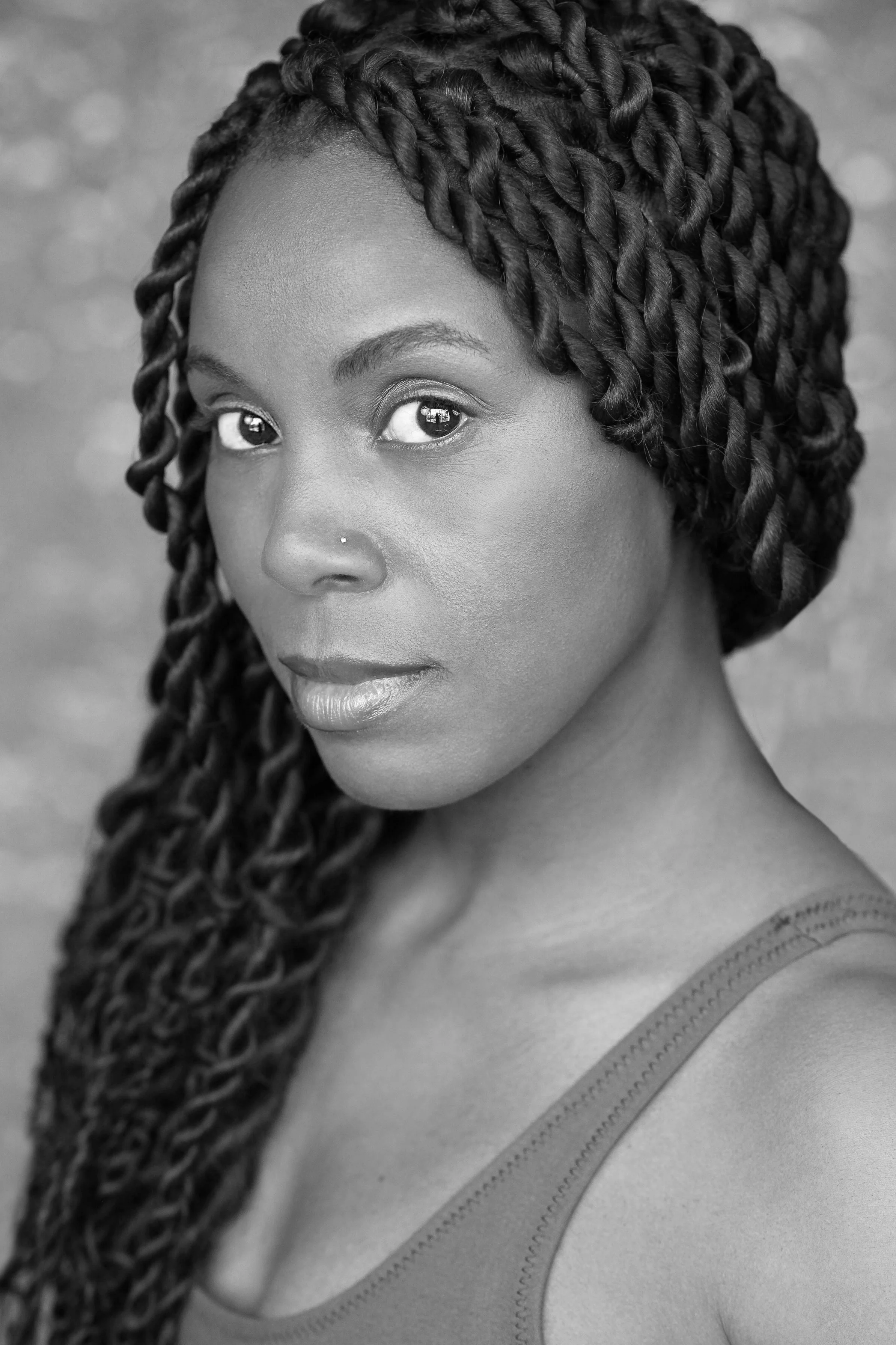 A black and white photo of a person with long black hair facing left and looking directly to camera.