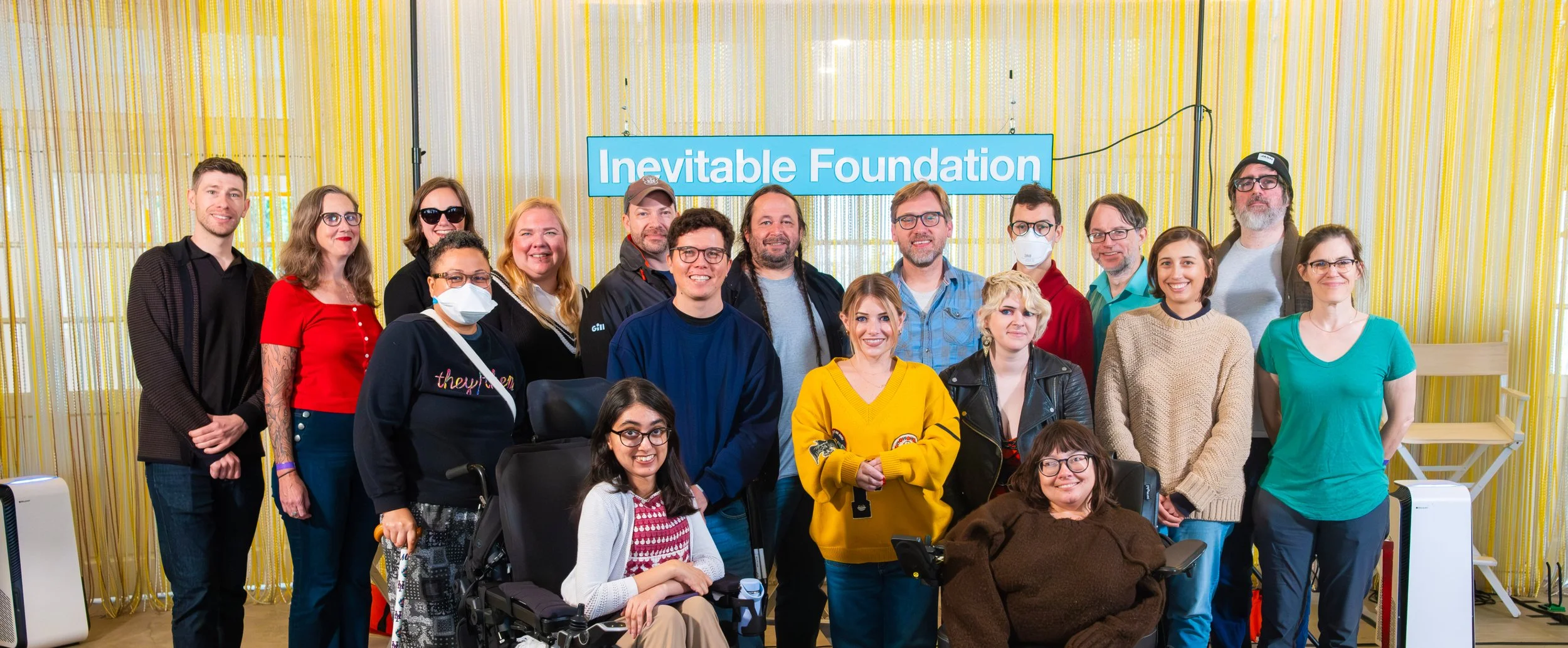 A group of Inevitable fellows against a yellow background and Inevitable Foundation sign