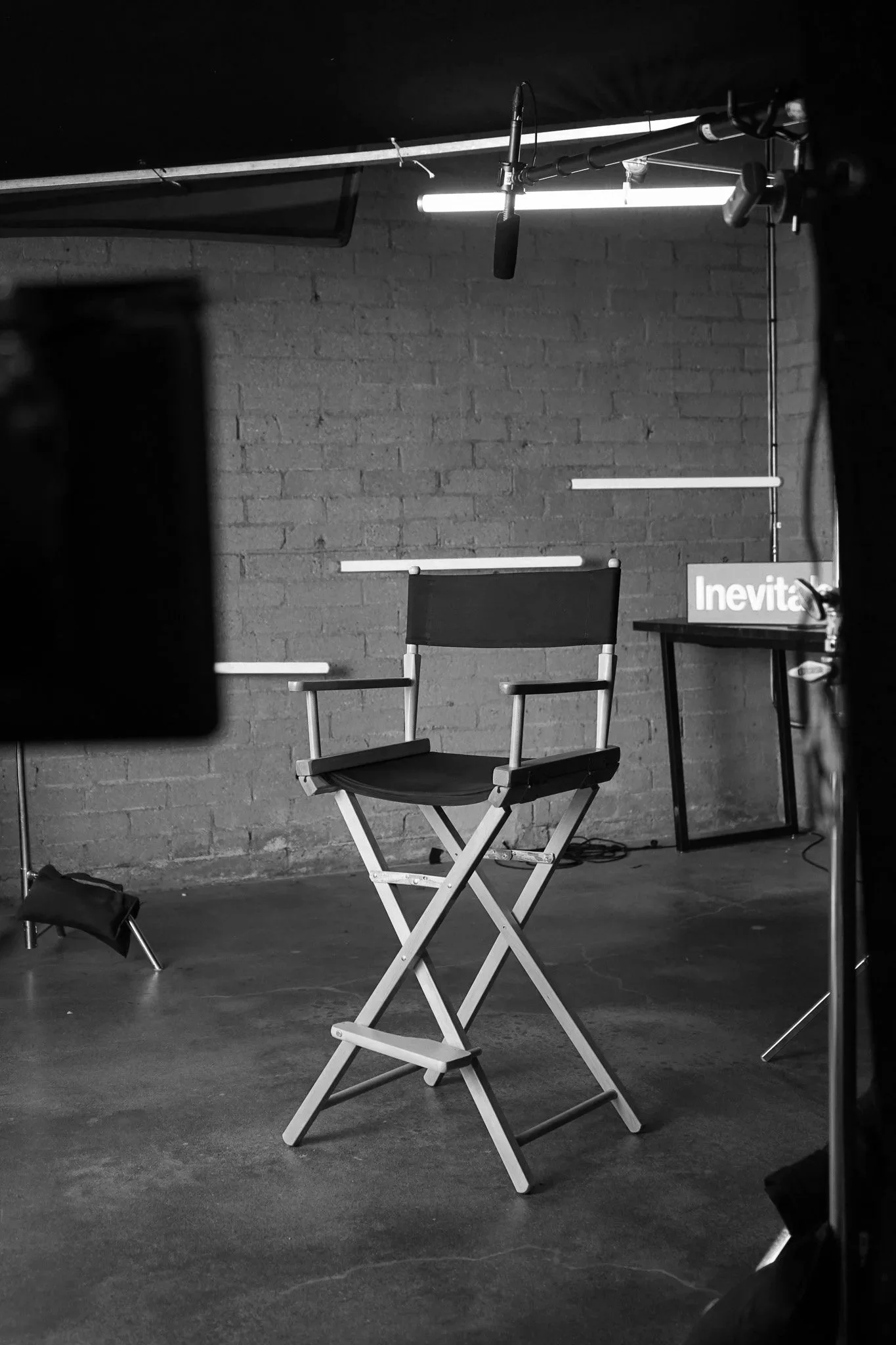 A director's chair unoccupied, against a brick wall with lights around it and an Inevitable Foundation sign.