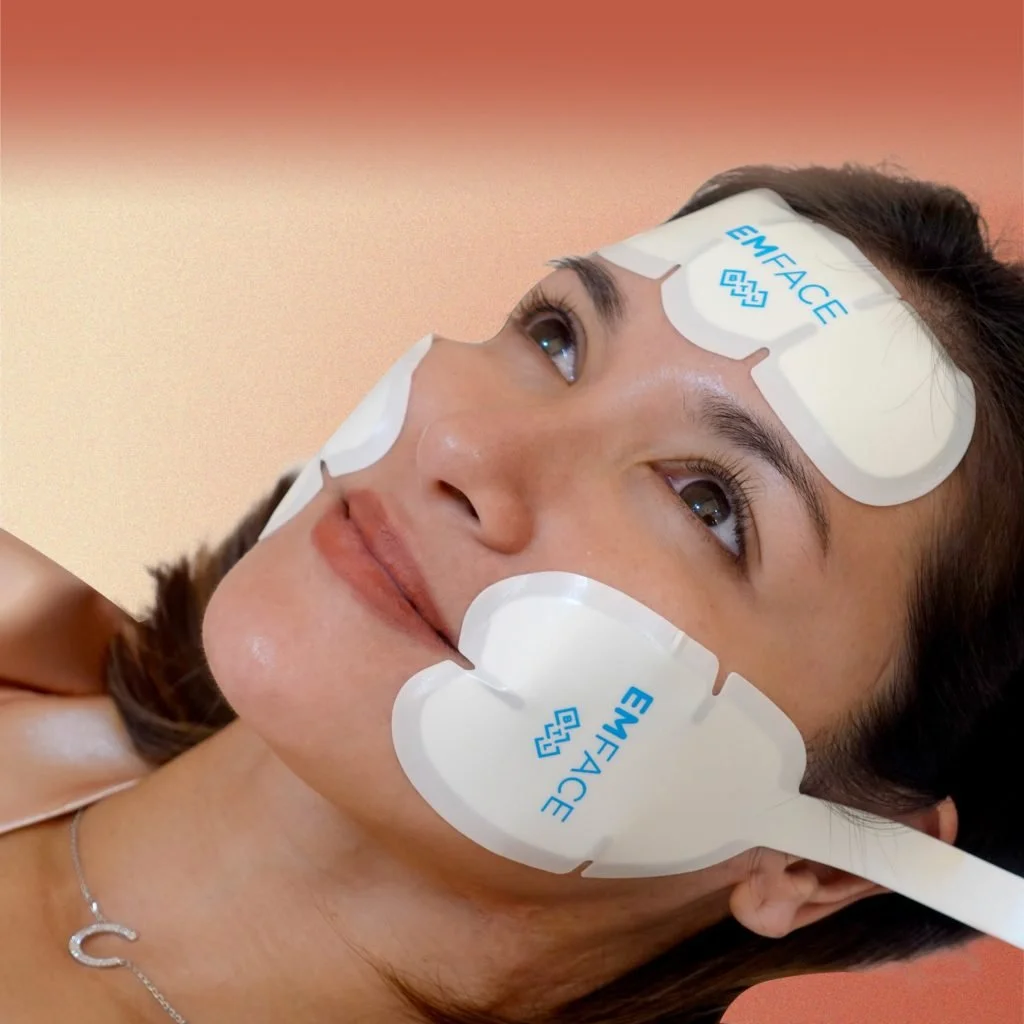 A woman lying down with patches on her forehead, cheeks, and chin, labeled "Emface," during a skincare treatment.