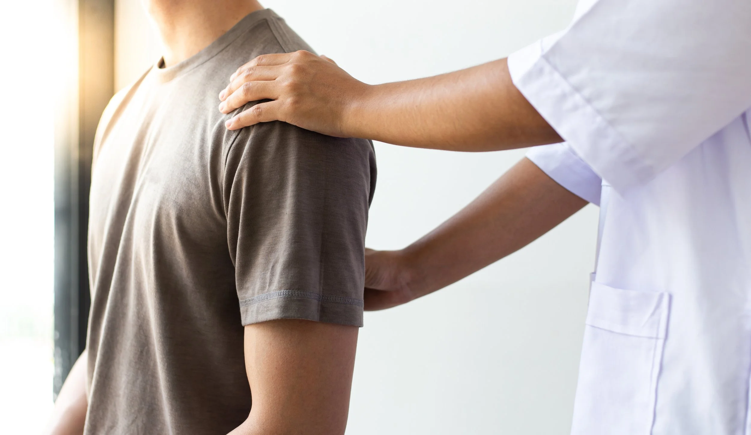 Healthcare professional placing hand on patient's shoulder during consultation.