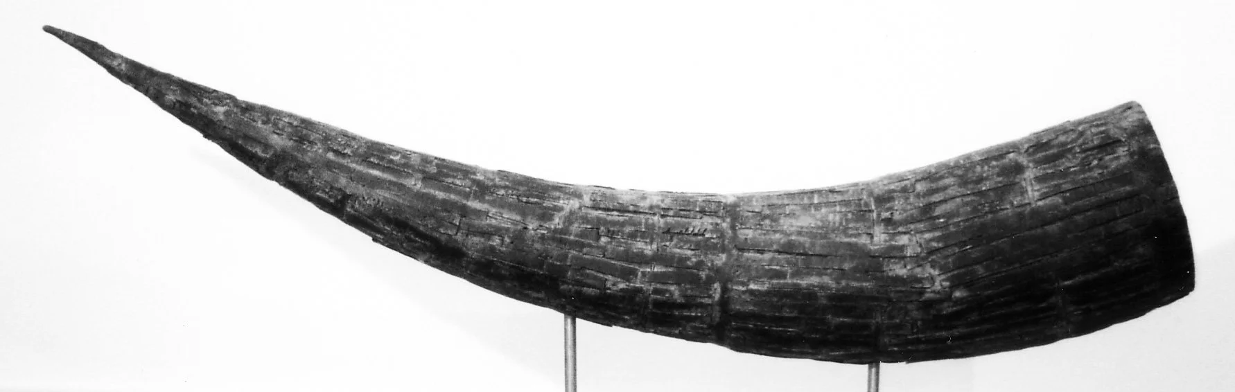 A bronze tusk displayed on a steel stand.