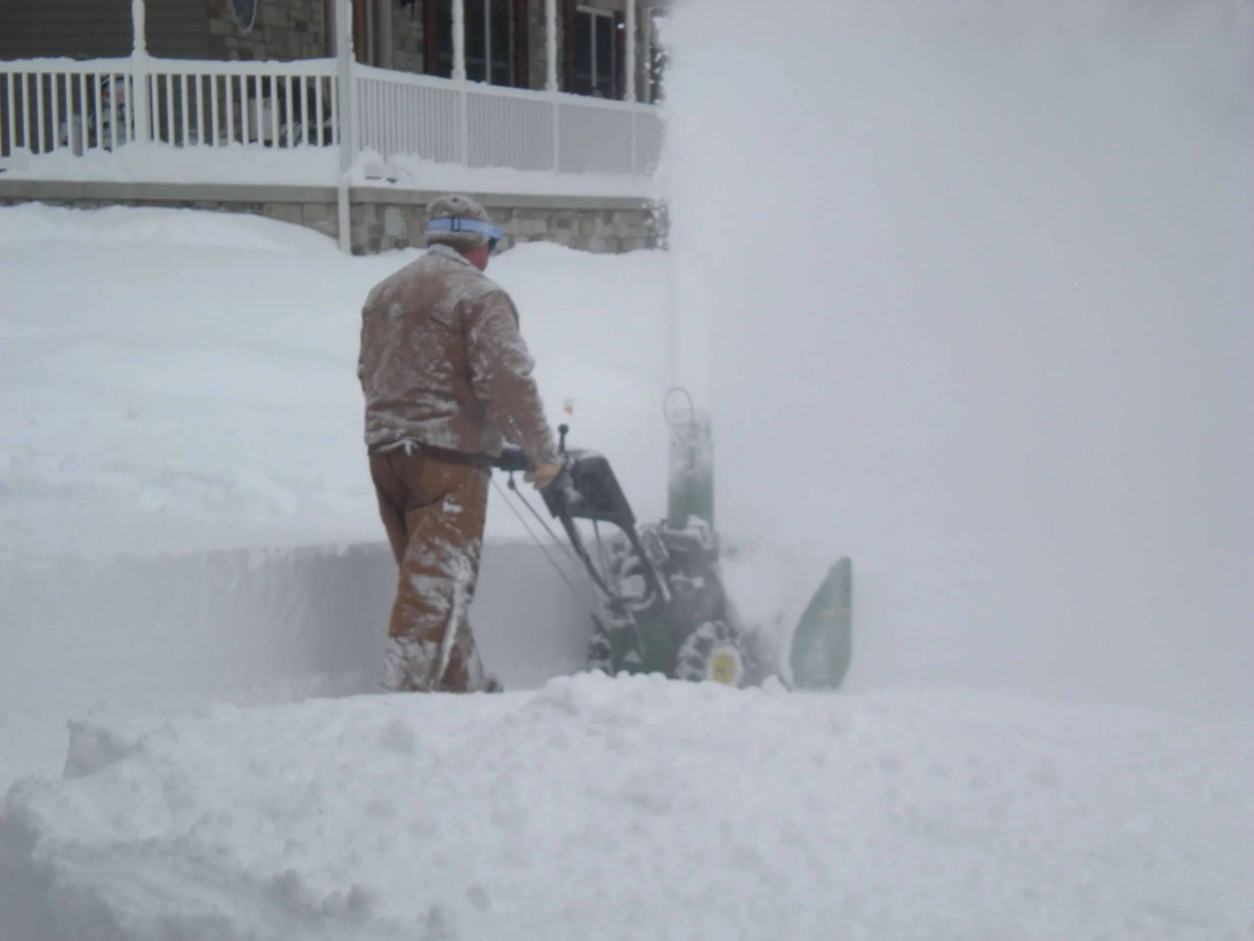 A person clearing snow from a driveway or sidewalk during a heavy snowstorm.