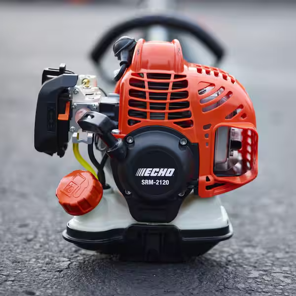 Close-up of a small, red and black gas-powered engine for outdoor equipment on a gray surface.