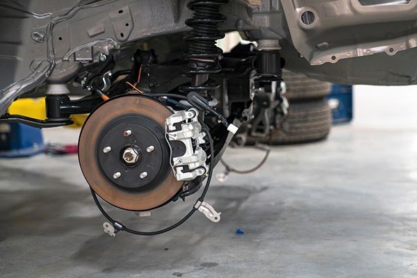 Close-up view of a car's brake system and suspension components with the wheel removed, showing the brake rotor, caliper, and mounting hardware.
