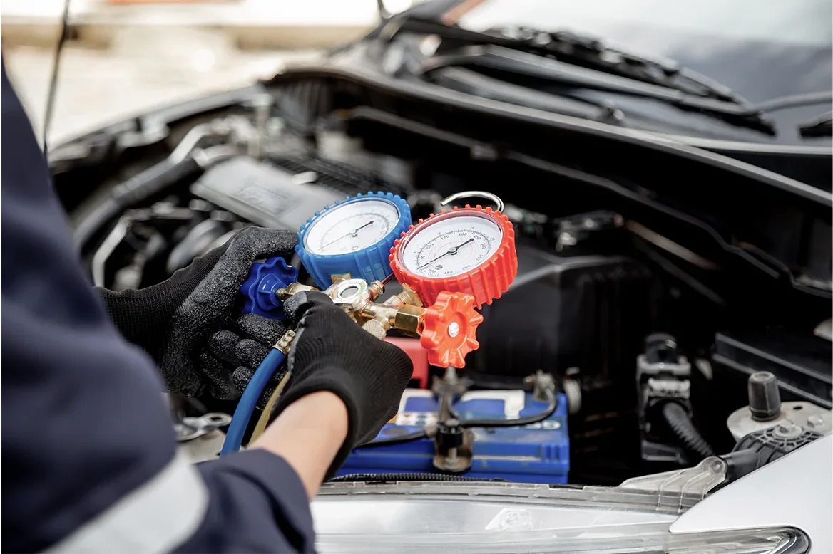 Person checking car engine pressure with manifold gauges.
