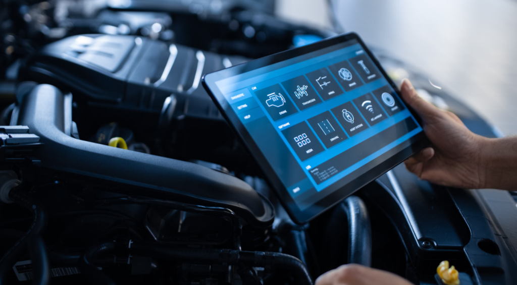 A person holds a tablet displaying diagnostic and control icons over a vehicle engine.