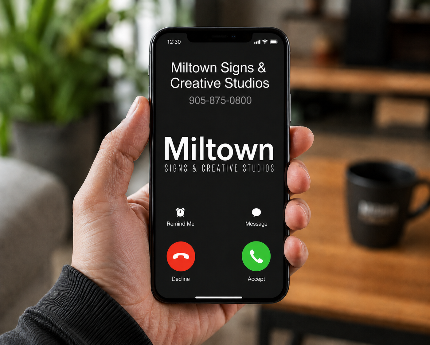 Hand holding a smartphone displaying an incoming call from MilTown Signs & Creative Studios.