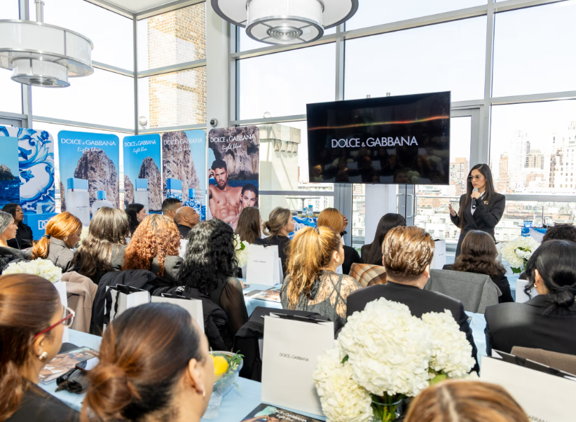 A woman giving a presentation to a group at a Dolce & Gabbana event in a high-rise building with large windows and city views.