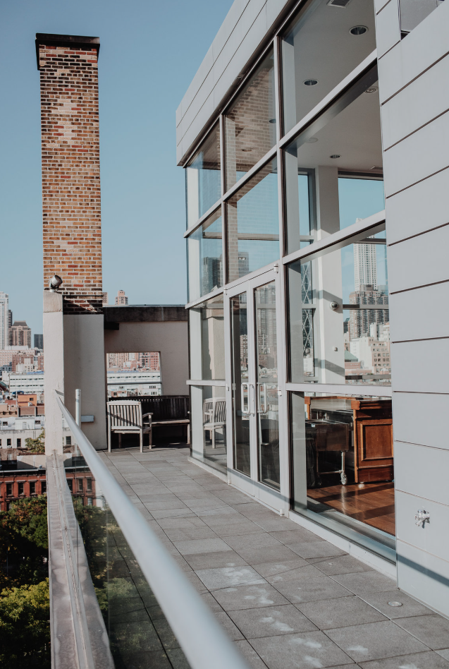 Balcony with glass railing and outdoor seating overlooking a city skyline with tall buildings in the background.