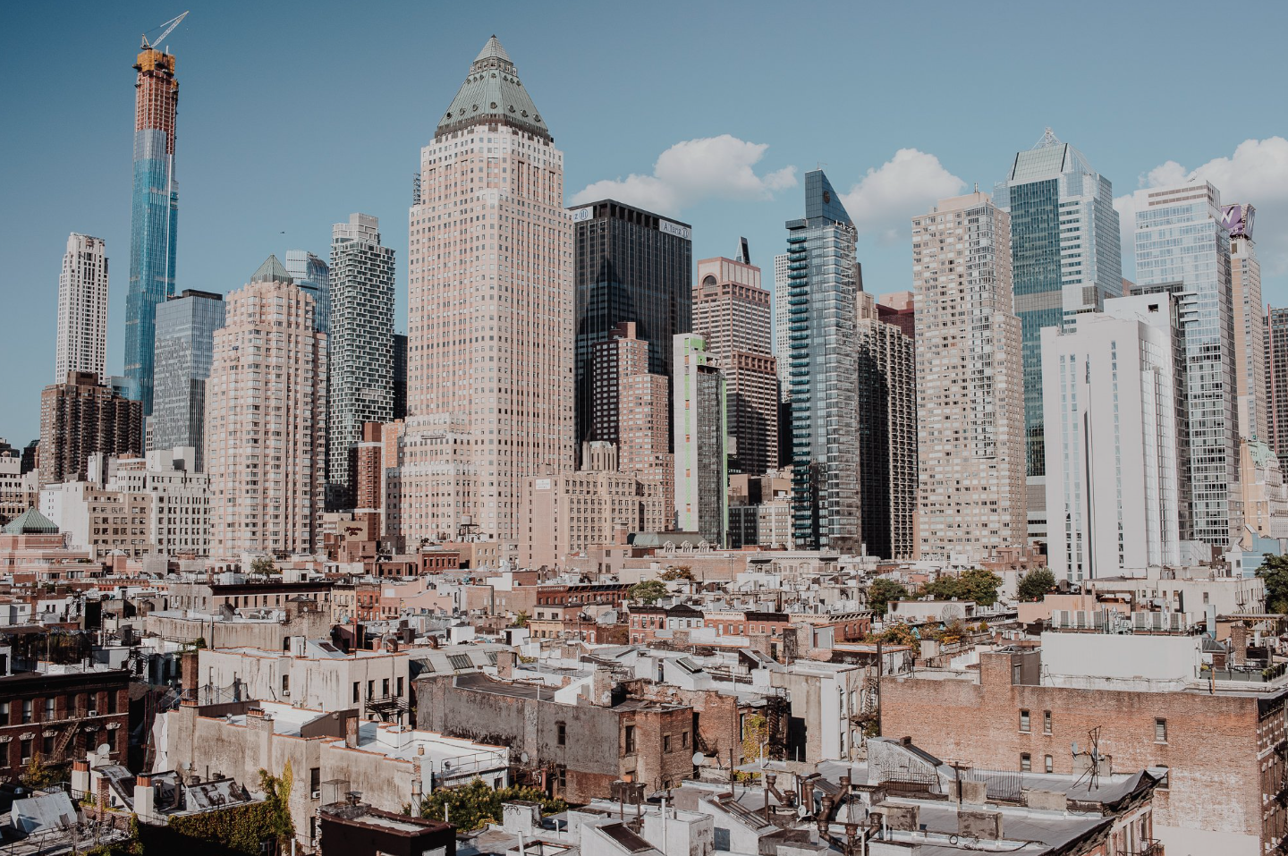 A cityscape of Manhattan with a mix of historic low-rise buildings in the foreground and modern skyscrapers in the background, under a partly cloudy sky.