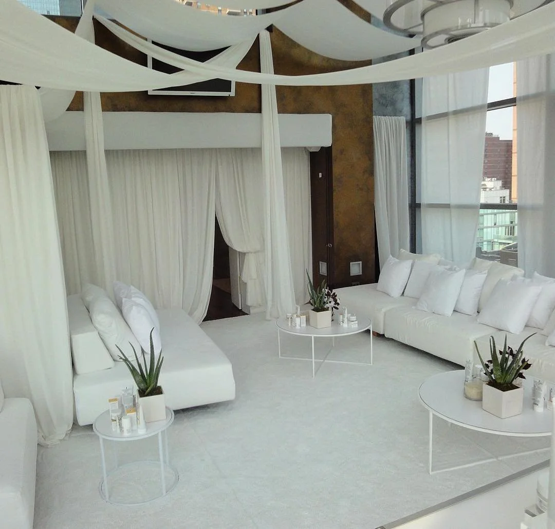 Elegant modern living room with white sofas, tables, and curtains, large windows with city view.