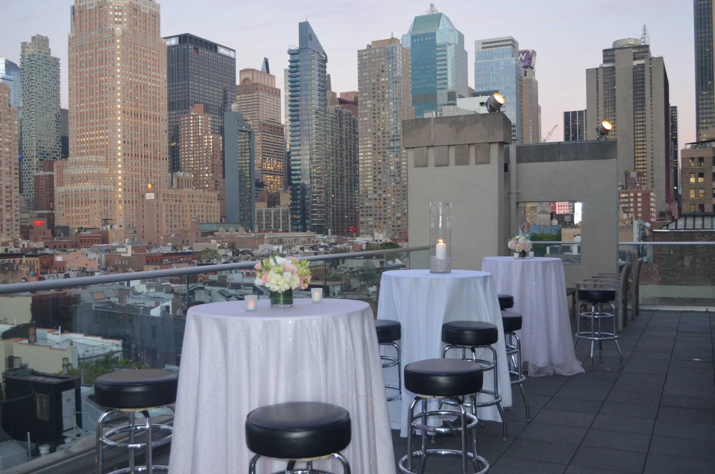 City skyline viewed from a rooftop with tables decorated with flowers and candles for an event.