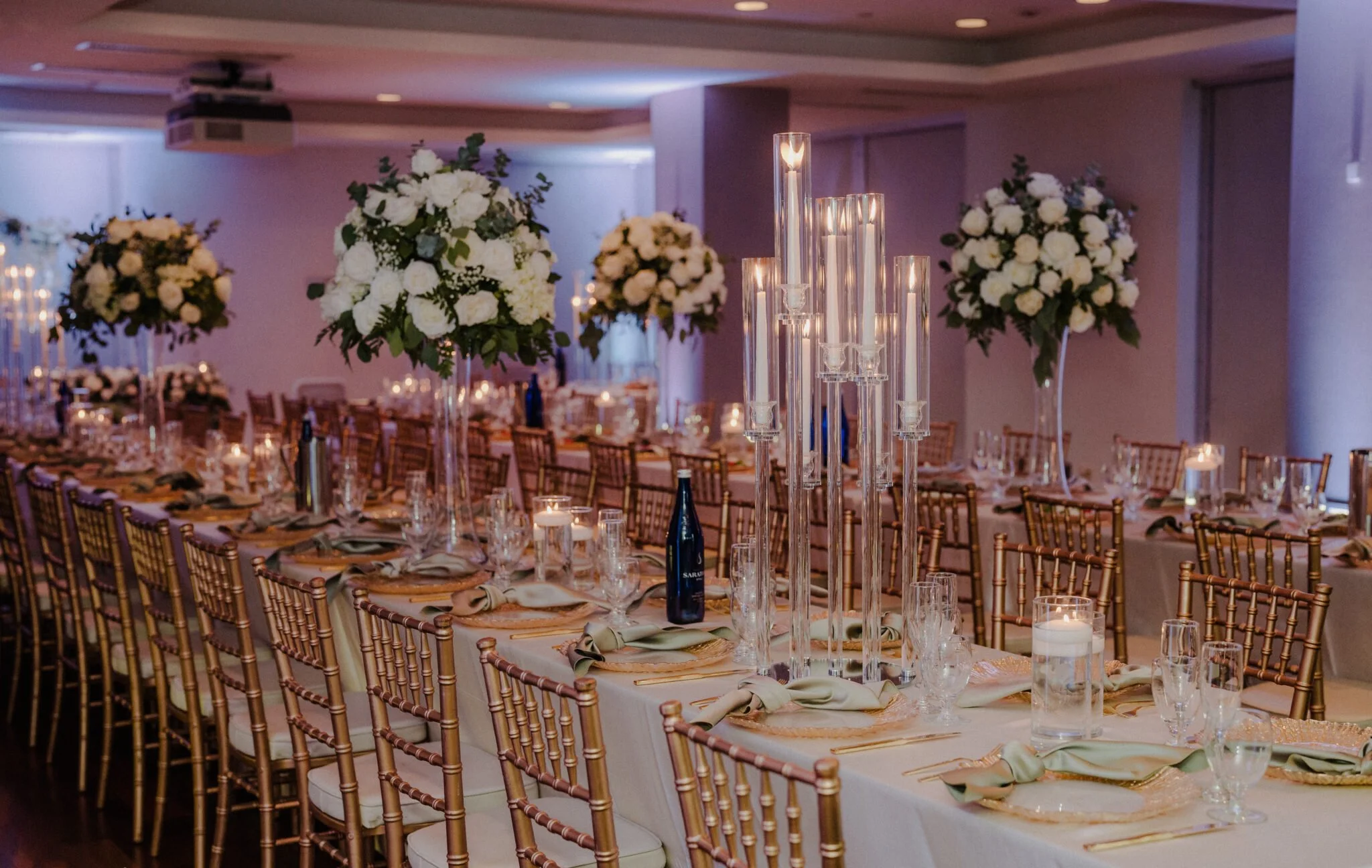 Elegant banquet hall decorated for a formal event with floral centerpieces and tall candleholders.