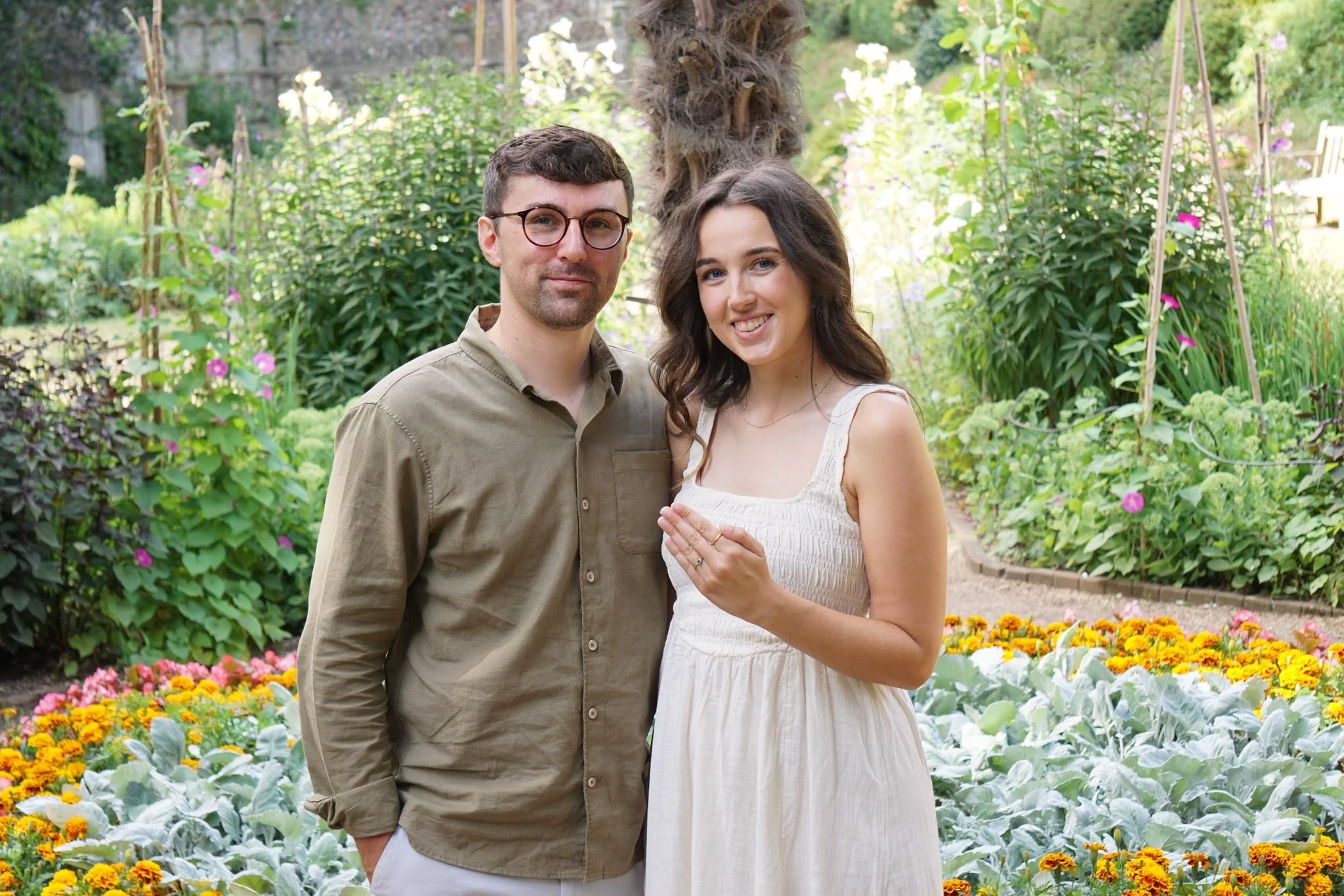 An engaged couple smiling together as the bride-to-be shows her ring during a garden pre-wedding photo shoot.