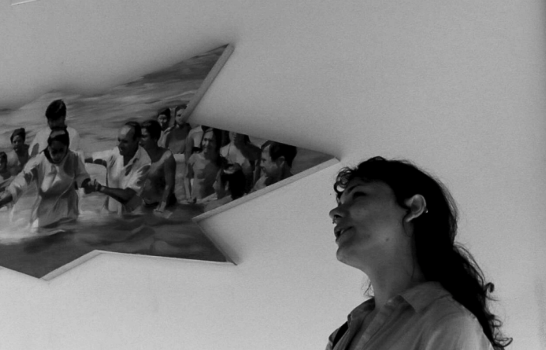 Mujer en primer plano con una pintura en la pared que muestra a un grupo de personas en el mar.