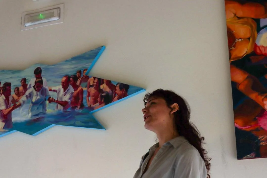 Mural en forma de estrella en la pared, con una imagen de personas en la playa, y una mujer de cabello oscuro y camisa clara en primer plano.