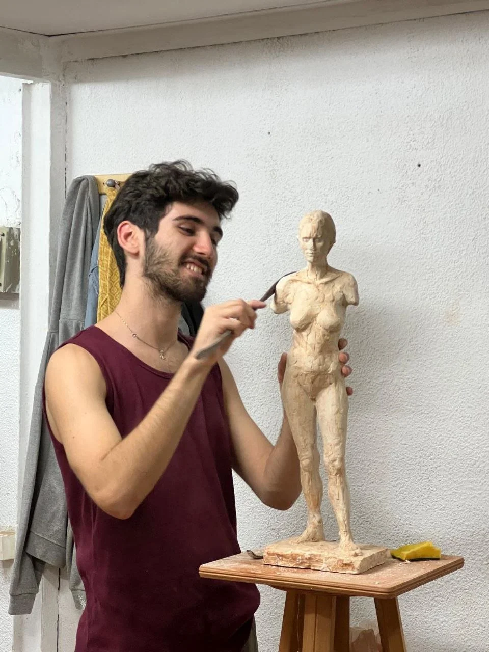 Joven esculpiendo una escultura de una figura humana femenina en arcilla en un taller, con una expresión de concentración y alegría.