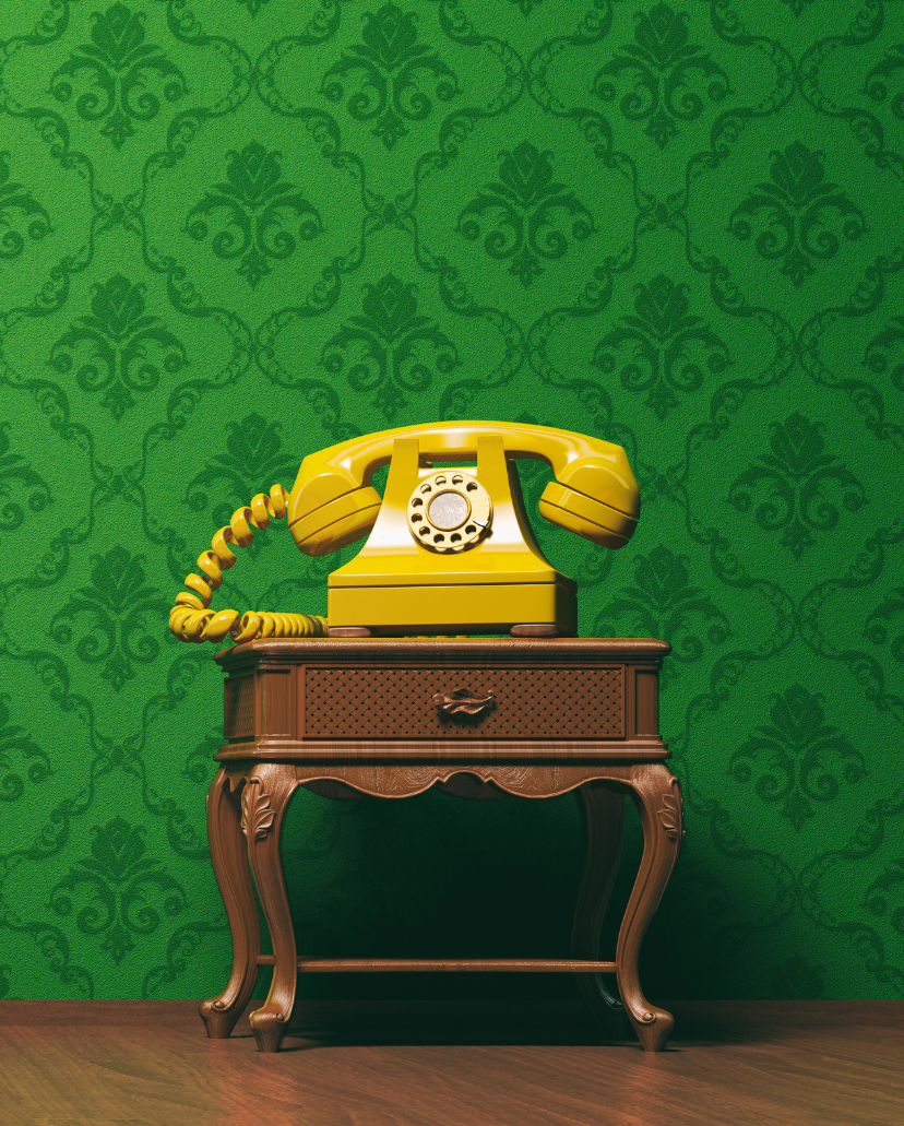 A vintage yellow rotary telephone on an ornate wooden table against a green patterned wallpaper background.