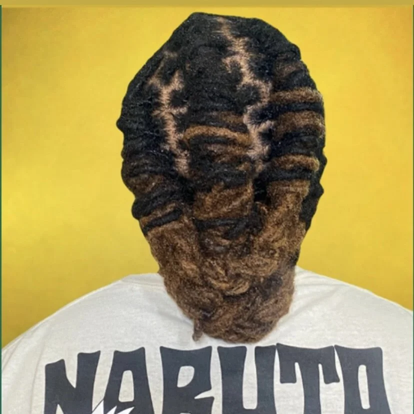 Close-up of a person's head with styled locs, dyed with dark and light brown colors, against a yellow background, wearing a white shirt with black text reading "NARUTO."