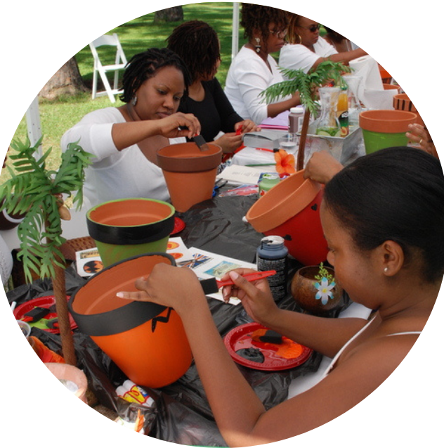 Group of women making and decorating Halloween-themed flower pots at a craft table outdoors.