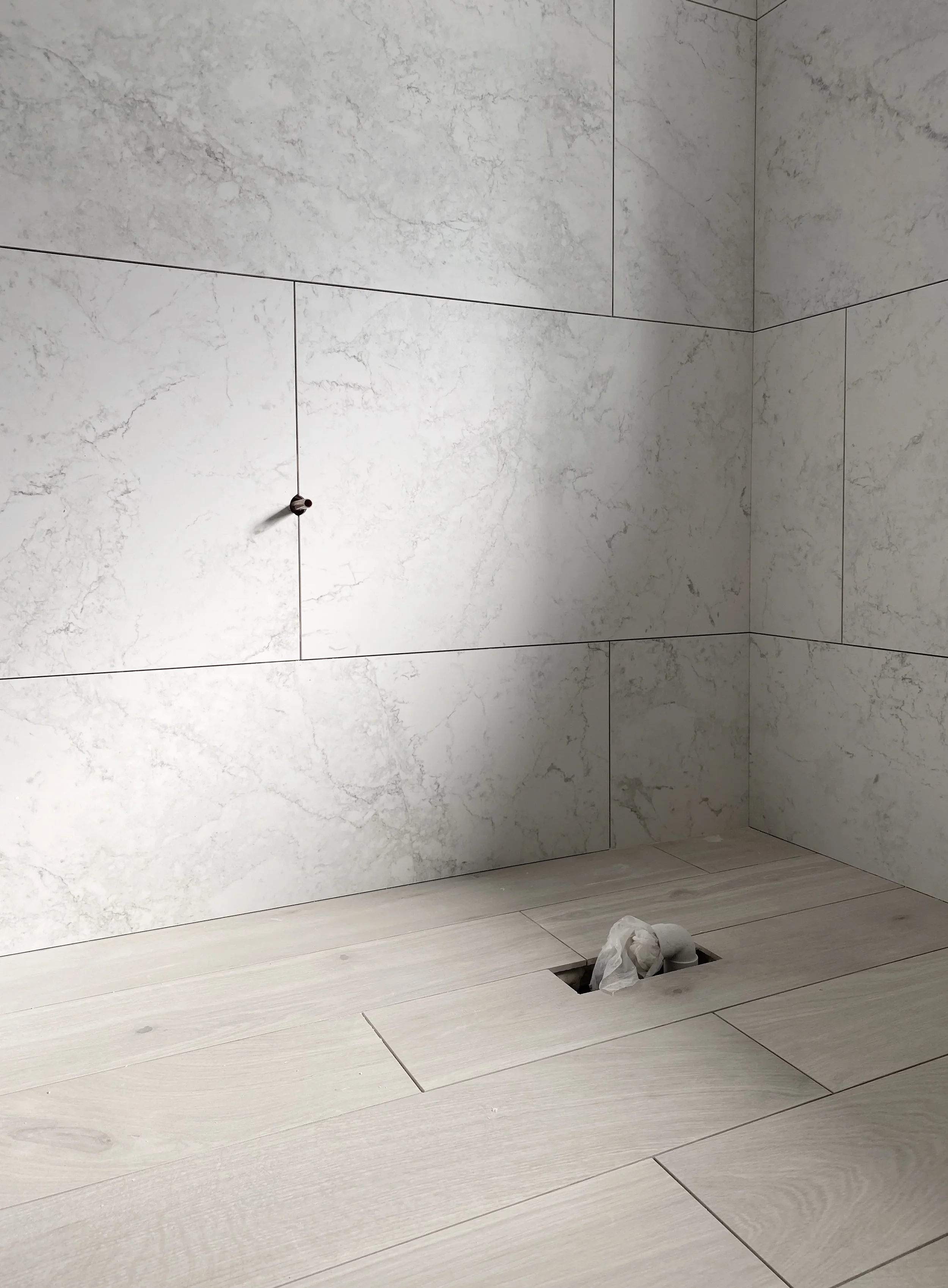 White marble-effect porcelain wall tiles and wood-look flooring during bathroom construction